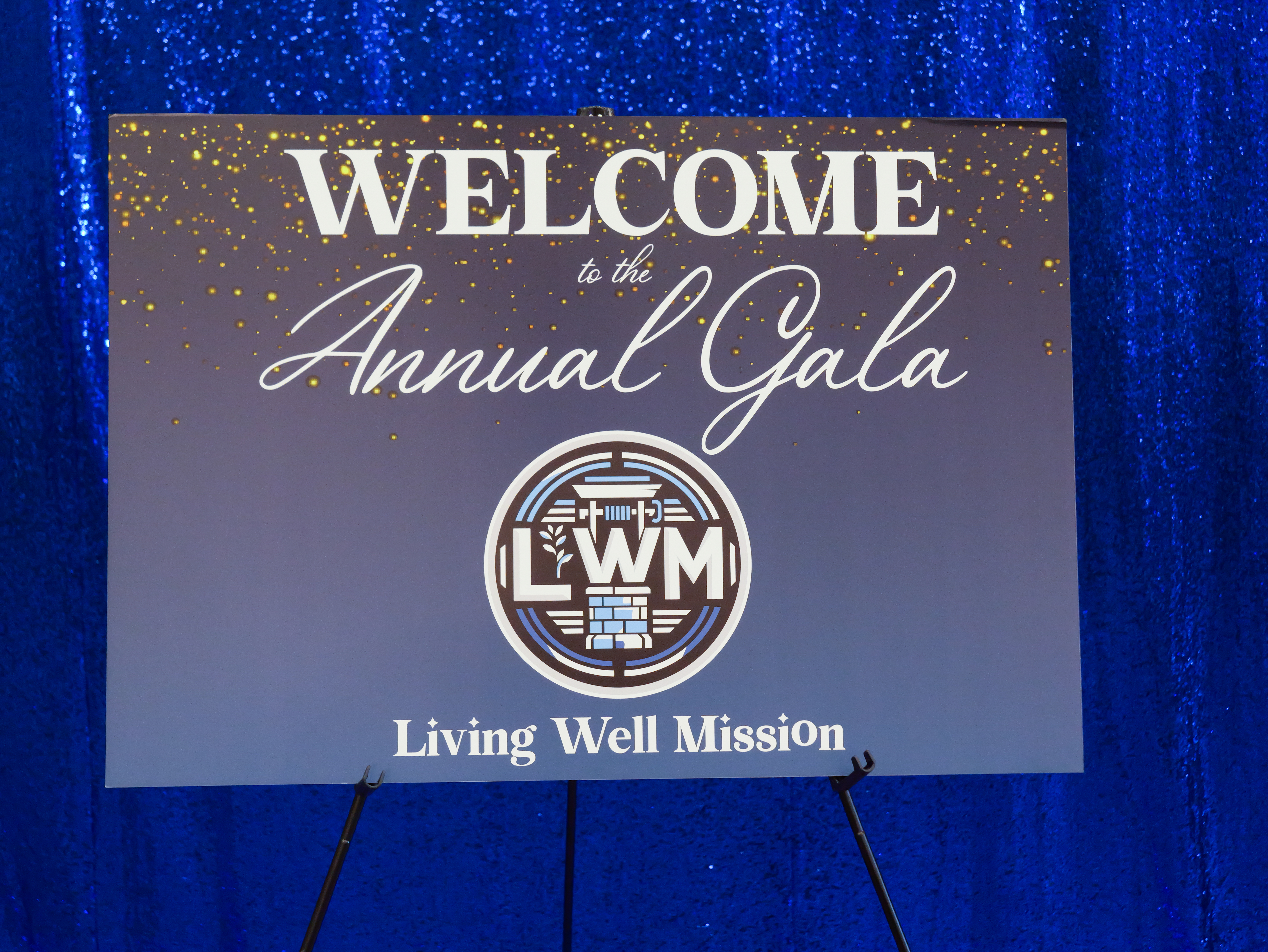 Welcome to the Annual Gala sign with Living Well Mission logo against a blue sequin backdrop