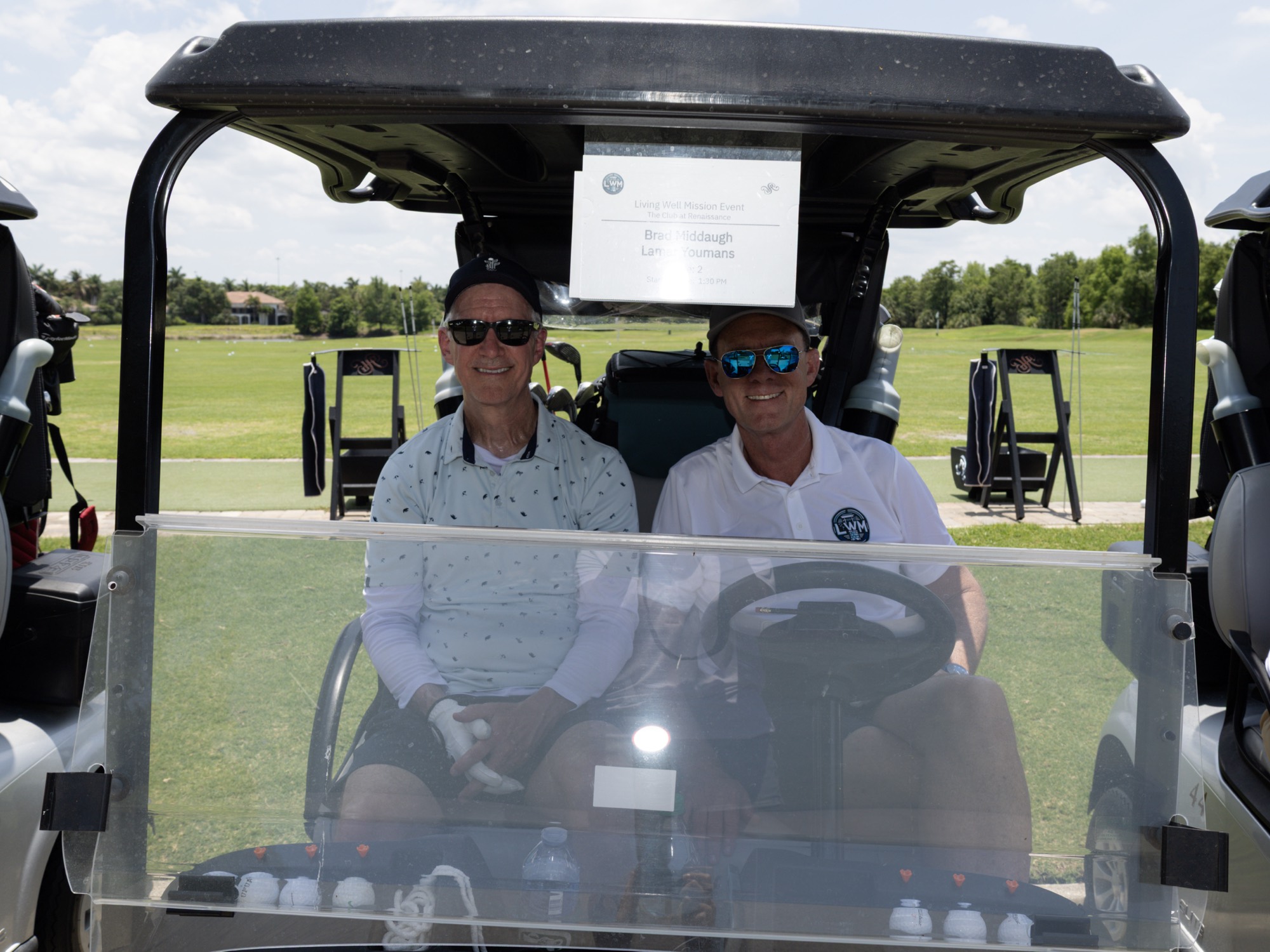 Two players grinning from their cart on the cart path